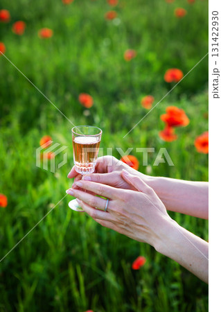 A woman's hands delicately hold a glass of rose wine in a poppy field, enjoying a summer's day A woman's hands delicately hold a glass of rose wine in a poppy field, enjoying a summer's day 131422930