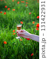A hand holds a glass of rose wine against a blurred background of a poppy field 131422931