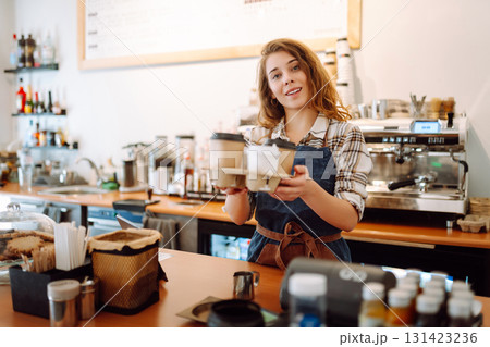 Portrait of a young woman barista holding takeaway coffee in hands. Takeaway food. Business concept. Portrait of a young woman barista holding takeaway coffee in hands. Takeaway food. Business concept. 131423236