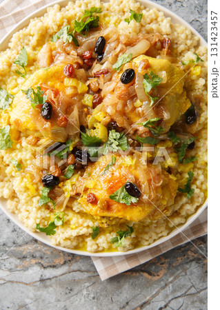 Chicken and Tfaya Couscous is a classic Moroccan dish in which tender couscous is topped with braised chicken and caramelized onion and raisin sauce closeup. Vertical top view 131423457