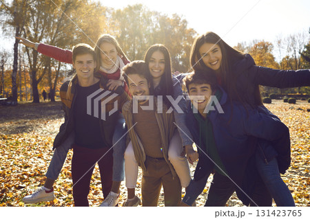 Group of young people piggybacking their girls while walking in a sunny autumn park together 131423765