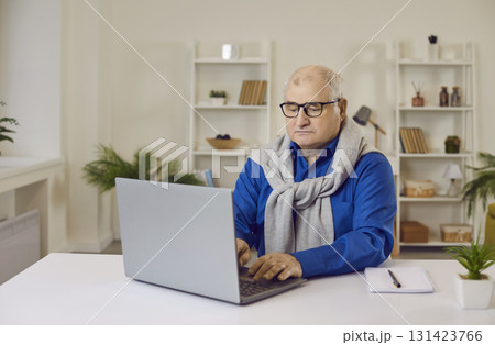 Old gray-haired senior mature man working using laptop sitting at the desk at home. Old gray-haired senior mature man working using laptop sitting at the desk at home. 131423766