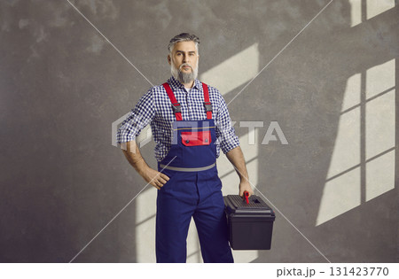 Portrait of senior male worker with toolbox standing on grey wall background at home Portrait of senior male worker with toolbox standing on grey wall background at home 131423770