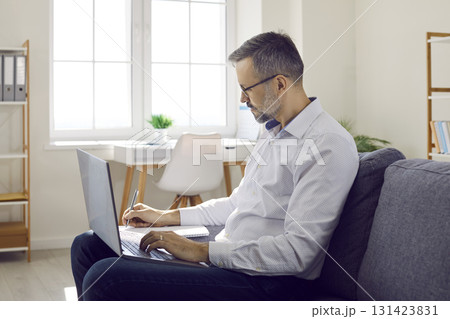 Middle aged businessman working with laptop and making notes Middle aged businessman working with laptop and making notes 131423831