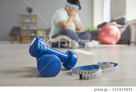 Overweight, obese upset woman sitting on floor with measuring tape 131423835