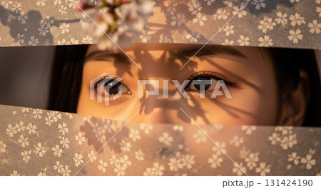 Asian woman eyes visible through horizontal gap in decorative floral patterned fabric with cherry blossom designs and warm golden sunlight shadows 131424190