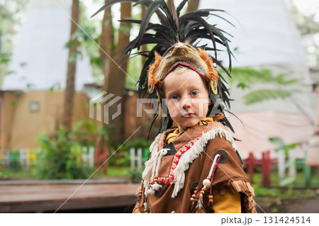 Portrait of a young boy wearing a traditional Indian feathered costume. The image was taken outdoors in a forest like setting, evoking a cultural or educational experience for children. Portrait of a young boy wearing a traditional Indian feathered costume. The image was taken outdoors in a forest like setting, evoking a cultural or educational experience for children. 131424514