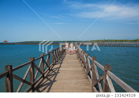 Family with children walks along a long wooden pier stretching into the blue sea on sunny day. Clear blue sky, calm ocean create peaceful, tropical atmosphere. Travel with kids, summer, beach vacation Family with children walks along a long wooden pier stretching into the blue sea on sunny day. Clear blue sky, calm ocean create peaceful, tropical atmosphere. Travel with kids, summer, beach vacation 131424519