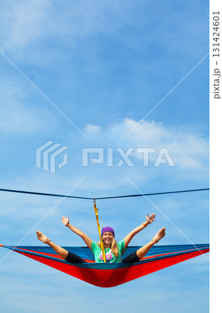 Young woman relaxing in hammock high above ground. A unique high-altitude attraction in Indonesia offering thrilling experiences and panoramic tropical forest views for adventure. Travel on vacation. Young woman relaxing in hammock high above ground. A unique high-altitude attraction in Indonesia offering thrilling experiences and panoramic tropical forest views for adventure. Travel on vacation. 131424601