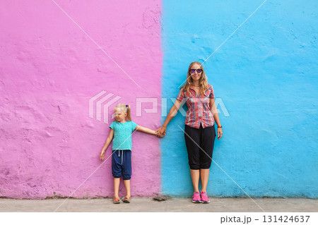Mother, daughter standing hand in hand against bright pink and blue wall in Kampung Warna Warni Jodipan. Fun and colorful travel. Family bonding, local culture and urban street art in Southeast Asia 131424637