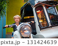 Smiling boy sits on a retro scooter museum. Funny moment during a family trip. Perfect for themes of travel on vacation, adventure, exploring, vintage vehicles, museums, family tourism. 131424639