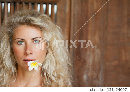 Young blonde woman with frangipani flower on open-air veranda of wooden bungalow in tropical garden. Girl relaxing in luxury villa on family summer vacation. Beach travel, spa, natural lifestyle. Young blonde woman with frangipani flower on open-air veranda of wooden bungalow in tropical garden. Girl relaxing in luxury villa on family summer vacation. Beach travel, spa, natural lifestyle. 131424697
