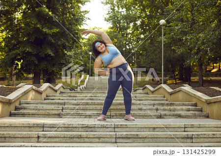Happy overweight woman doing fitness exercises on stone stairway in beautiful city park Happy overweight woman doing fitness exercises on stone stairway in beautiful city park 131425299