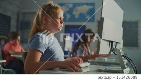 Blonde Girl in Blue Shirt Works on Desktop Computer While Classmates Sit at Desks Blonde Girl in Blue Shirt Works on Desktop Computer While Classmates Sit at Desks 131426089
