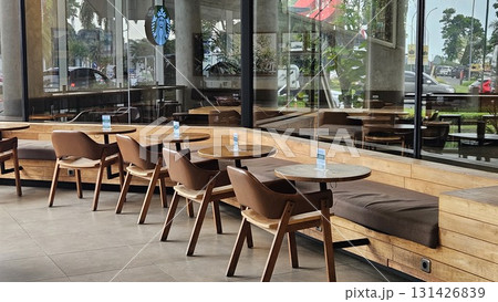 This spacious and modern cafe features smooth concrete walls and tiled flooring, creating an industrial-chic atmosphere where warm wooden tables and comfortable leather chairs are arranged along long, This spacious and modern cafe features smooth concrete walls and tiled flooring, creating an industrial-chic atmosphere where warm wooden tables and comfortable leather chairs are arranged along long, 131426839