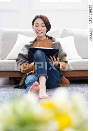 ワイヤレスイヤホンをつけてタブレットを使用するミドル女性 131426926