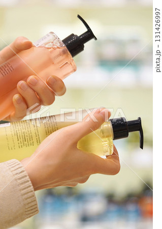 Vertical screen. Customer compares haircare, self care, skincare products in a cosmetics aisle. Woman reads labels and ingredients. Closeup female hands holds two different bottles. Conscious choice Vertical screen. Customer compares haircare, self care, skincare products in a cosmetics aisle. Woman reads labels and ingredients. Closeup female hands holds two different bottles. Conscious choice 131426997