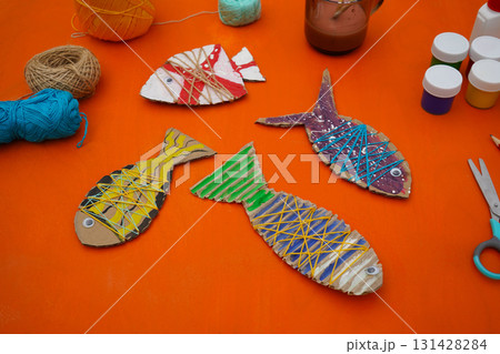 Assemble a fish using cardboard, thread, and paint, with clear instructions, against an orange background. Assemble a fish using cardboard, thread, and paint, with clear instructions, against an orange background. 131428284