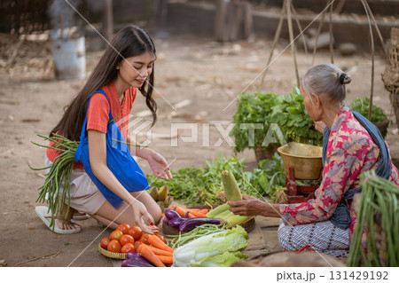 A young woman happily buying fresh produce from an elderly seller at the market today 131429192