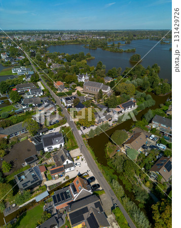 Aerial view of a small town with a central church and tall steeple, surrounded by houses, tree lined streets, and nearby lakes with islands, blending historic charm and natural beauty. Aerial view of a small town with a central church and tall steeple, surrounded by houses, tree lined streets, and nearby lakes with islands, blending historic charm and natural beauty. 131429726