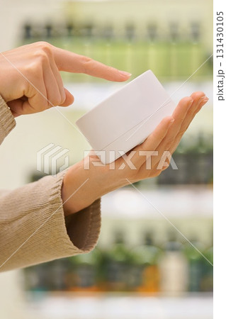 Vertical shoot. Woman holding a cosmetic jar in a beauty store, reading the label, examining ingredients. Moisturizing anti-aging face cream, hair mask. Concept of conscious choice, skincare, haircare 131430105