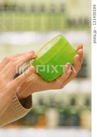 Close up of woman holding a jar in a beauty store, reading label and ingredients. Female shopper examining cosmetic product before purchase. Concept conscious choice for skincare, haircare products. 131430109