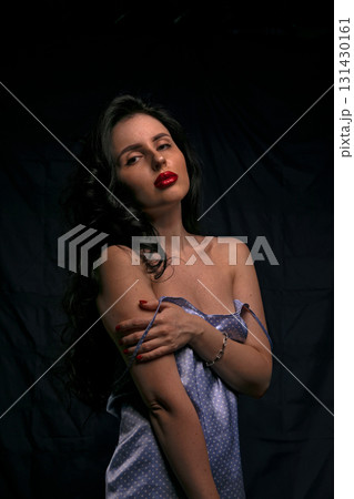 woman stands elegantly with her arms crossed wearing a light blue outfit. Her dark hair cascades around her shoulders and she gazes confidently at the camera in a studio setting. 131430161