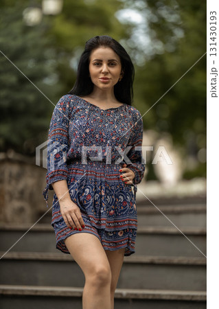 woman stands confidently on staircase steps in a vibrant dress enjoying a sunny day in a green park. The lush foliage creates a serene atmosphere. woman stands confidently on staircase steps in a vibrant dress enjoying a sunny day in a green park. The lush foliage creates a serene atmosphere. 131430193