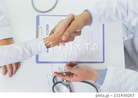 Top view shot of doctor and patient shaking hands at office desk in hospital. Healthcare and medicine banner. Doctor shaking hands with patient after talking about medical examination results. Top view shot of doctor and patient shaking hands at office desk in hospital. Healthcare and medicine banner. Doctor shaking hands with patient after talking about medical examination results. 131430267