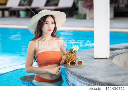 Sexy young asian woman in swimsuits in summer. beautiful woman in orange bikini with hat and tropical drink in swimming pool. Sexy young asian woman in swimsuits in summer. beautiful woman in orange bikini with hat and tropical drink in swimming pool. 131430332