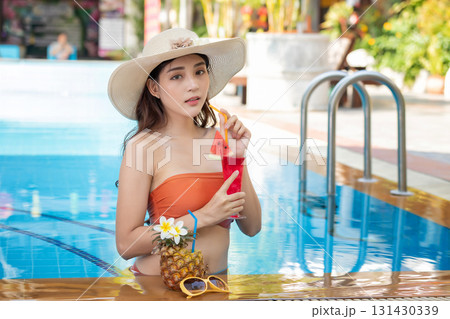 Sexy young asian woman in swimsuits in summer. beautiful woman in orange bikini with hat and tropical drink in swimming pool. 131430339