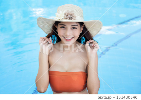 Sexy young asian woman in swimsuits in summer. beautiful woman in orange bikini and hat in swimming pool with tropical drink. 131430340