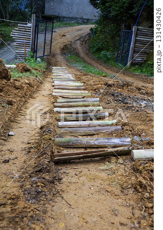 The road is unpaved, with a mix of dirt and small wooden planks, and it curves gently to the right.The mood is serene and rustic, evoking a sense of adventure or exploration in a natural setting. The road is unpaved, with a mix of dirt and small wooden planks, and it curves gently to the right.The mood is serene and rustic, evoking a sense of adventure or exploration in a natural setting. 131430426