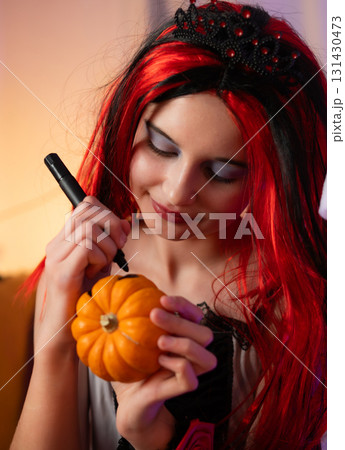 Cute Little Girl In A Halloween Witch Wig Plays With A Pumpkin And Draws A Face For Festive Decorations Cute Little Girl In A Halloween Witch Wig Plays With A Pumpkin And Draws A Face For Festive Decorations 131430473