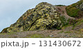 large moss and lichen covered rock formation on a steep hillside, surrounded by green grass and a winding dirt path leading into the natural landscape, beauty and tranquility of nature 131430672