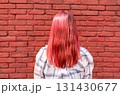 rear view of young woman with vibrant red pink hair stands against textured red brick wall, showcasing a casual style and modern fashion, embodying youthful energy and individuality 131430677