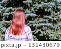 Young woman with long red hair, wearing a plaid shirt, stands in front of lush evergreen spruce trees, enjoying nature and reflecting on her surroundings in serene outdoor setting, copy space 131430679