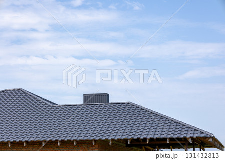 A modern roof with gray tiles under a bright blue sky, showcasing a clear day and attention to construction details 131432813