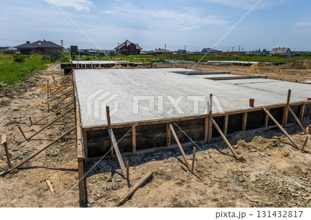 Workers are pouring concrete for a foundation at a construction site on a clear day, surrounded by new homes and green fields Workers are pouring concrete for a foundation at a construction site on a clear day, surrounded by new homes and green fields 131432817