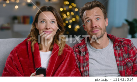 Happy couple watching television at home during winter holiday season on cozy sofa 131433014