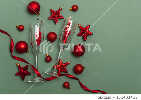 Champagne Flutes with Red Christmas Ornaments and Ribbon on Green Background Champagne Flutes with Red Christmas Ornaments and Ribbon on Green Background 131433415