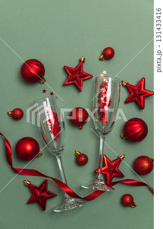 Champagne Flutes with Red Christmas Ornaments and Ribbon on Green Background Champagne Flutes with Red Christmas Ornaments and Ribbon on Green Background 131433416