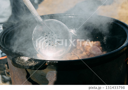 Meat cooking in a large cauldron outdoors over an open fire, a classic outdoor cooking concept for camping and traditional cuisine. 131433798