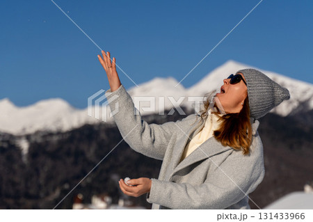 Snowball Mountains Winter: Woman playfully throws snowball amidst scenic snowy mountain range during winter. 131433966