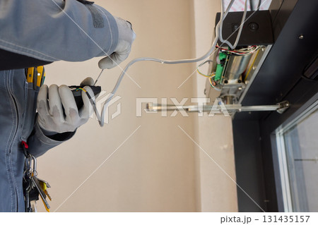 A technician is repairing an advanced automated door system with electrical tools A technician is repairing an advanced automated door system with electrical tools 131435157
