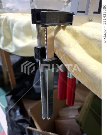 Clamps firmly hold an aluminum corner in a workshop. The setup shows the tools being used for assembly. Various materials and equipment are present around the workspace. 131435380