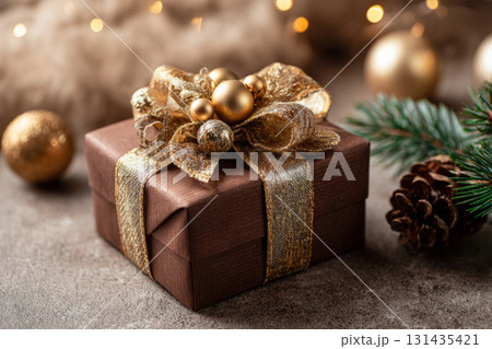 Brown gift box decorated with golden ribbon and pine cones on blurred festive lights background Brown gift box decorated with golden ribbon and pine cones on blurred festive lights background 131435421