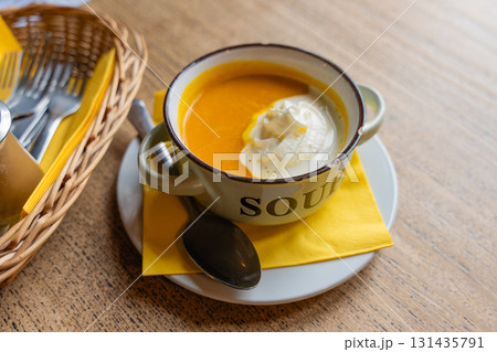 Rustic pumpkin soup served in enamel mug with chipped edge on wooden table. Cottage core Rustic pumpkin soup served in enamel mug with chipped edge on wooden table. Cottage core 131435791