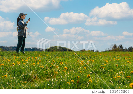 Woman checking phone navigation in spring dandelion meadow in Czech countryside Woman checking phone navigation in spring dandelion meadow in Czech countryside 131435803