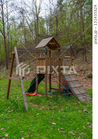 Wooden playground set with swing, slide, and climbing rope in forest park setting during spring 131435824